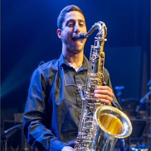 Our story saxophonist image: young musician playing saxophone on stage, "From a Vision to a Cultural Beacon" at Yizre'el Gilboa Music Center